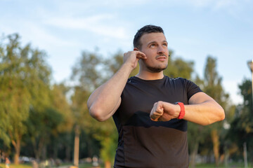 Fototapeta premium Young man jogging in park. Having a break and using his smart watch