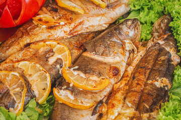 Baked fish stuffed with lemon and vegetables on a charcoal grill with shallow depth of field. Fried fish on a plate with tomato and salad.