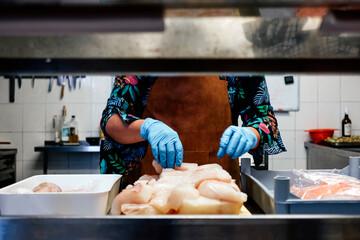 woman in restaurant kitchen cutting and preparing slices of fish