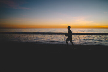 Fototapeta premium Męska sylwetka joggera rozpoczynającego dzień z aktywnością w porannym zmierzchu na linii brzegowej oceanu, mężczyzna biegający po piaszczystej plaży o zmierzchu i zachodzie słońca spędzający letnie wakacje na tropikalnej wyspie
