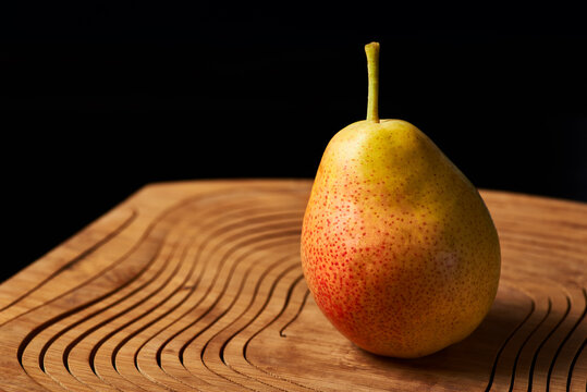 The red-yellow pear lies on a wooden stand on a black background