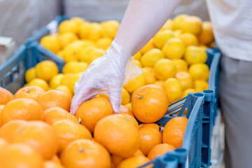 Shopper wearing protective gloves choosing oranges during the coronavirus epidemic or flu outbreak