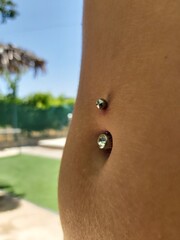 Navel piercing in female belly. small hairy belly with a blurred background. Blurred pool bottom....