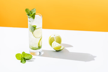 Fresh Mojito cocktail with lime and mint in highball glass with water drops on white and yellow background in bright sun light, Mojito refreshing drinks. Copy space, summer vacation and party concept