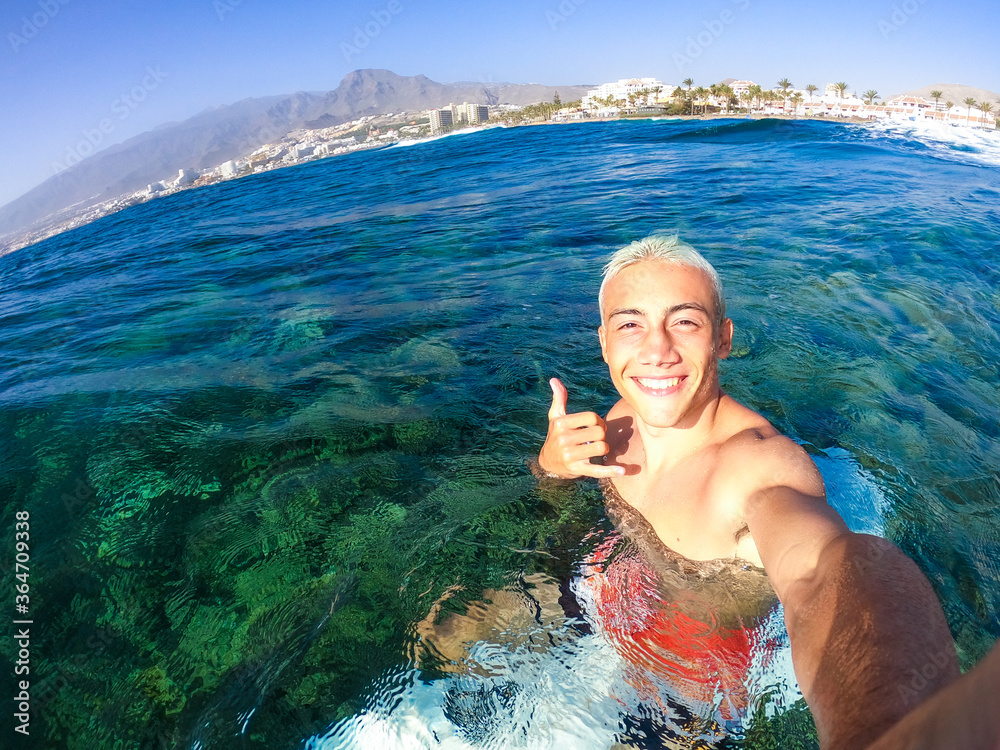 Wall mural one teenager man enjoying surfing lifestyle at the beach in the sea or ocean - happy and handsome millennial smiling and looking at the camera - adult having fun at summer in his vacations holiday 