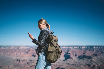 Young girl wanderlust with rucksack getting notification on telephone using data roaming connection during hiking tour,female traveler reading new message on cellphone standing on top in Grand canyon.