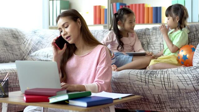 A Beautiful Asian Mother Busy Working From Home While Looking After And Teaching Her Children Home Work On A Laptop Computer