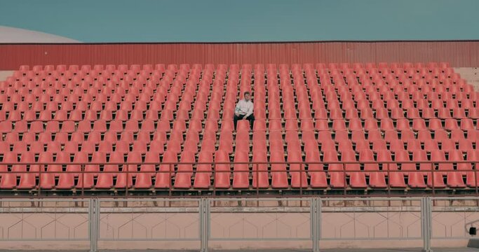 Wide view of a lonely fan attending a sports event on an empty stadium. Events during coronavirus pandemic concept. Lonely man on the empty stadium seat cheering for the team and applauds the players.