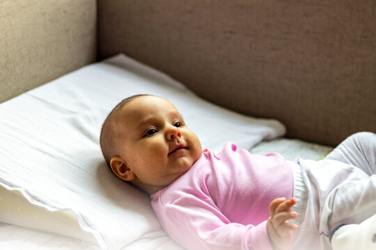 Shot of three month old infant.Portrait of baby on the bed in her room.Adorable baby bonding with her mother at home.Giggles,cuddles and snuggles.Color photo of laughing baby lying on textured pillow.