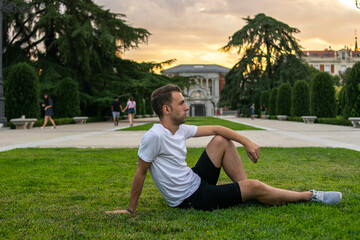 Photo of a young and attractive man sitting relaxed on the grass looking to the horizon