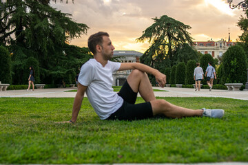 Photo of a young and attractive man sitting relaxed on the grass looking to the horizon