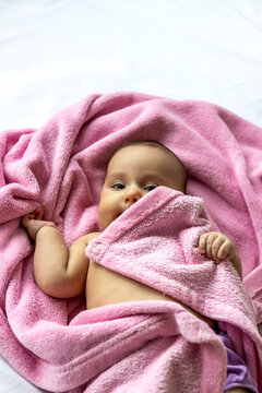 Photo of pretty chubby baby girl portrait, in diaper pants,lying in bed wrapped in soft pink blanket.Looking up.Caucasian baby girl looking at camera.Portrait of lovely baby wrapped in pink blanket.