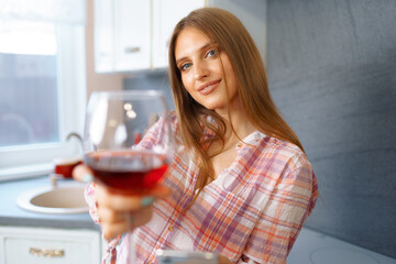 Blonde caucasian woman with glass of red wine standing in her kitchen