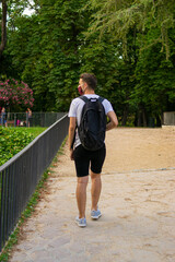 Photo of a young and attractive man with a backpack wearing a reusable face mask walking in the park doing tourism