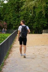 Photo of a young and attractive man with a backpack wearing a reusable face mask walking in the park doing tourism