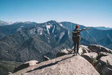 Back view of female hiker standing on top of mountain exploring mountains and landscape pointing, 20s woman explorer showing destination for wanderlust during active leisure in national park