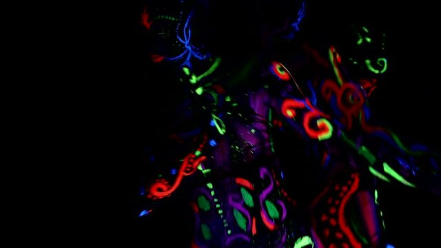 Woman dances in ultraviolet  neon light, her body painted with colored paints