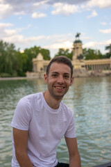 Photo of a young and attractive man with a white t/shirt standing next to the lagoon in Retiro park, Madrid