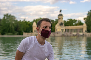 Photo of a young and attractive man wearing a face mask and sitting next to a beautiful and graan park isolated in nature