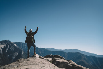 Obraz premium Freedom concept of male explorer excited with getting to mountain top achievement on hiking tour,happy guy wanderlust with backpack celebrating victory on high rock cliff amazed with