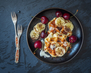 Sweet dessert for a delicious snack. Wafers with bananas, chocolate and cherries on a black plate
