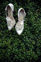 A pair of white elegant bride shoes on a green bush background