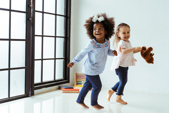 Candid portrait of two energetic playful young diverse friends children playing indoors. African American and Caucasian girls together