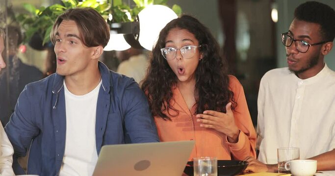 Young colleagues making surprised face while looking at laptop screen. Millennial amazed startupers having good news while sitting in cafe. Concept of success and teamwork.