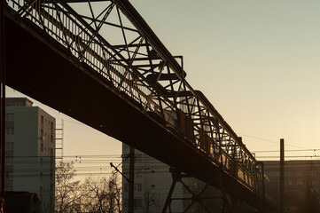 Metal footbridge over the railway seen at sunset in a diagonal perspective.