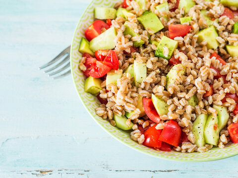 Fresh Italian farro spelt salad with tomatoes, avocado and cucumbers on wooden turquoise board. Easy recipe whole food meal