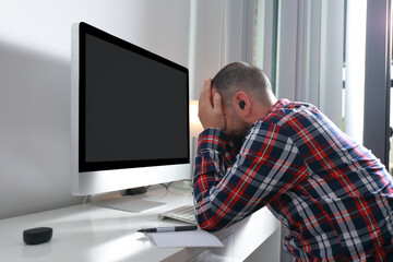 Desperate young man with hands on face in front of computer at work