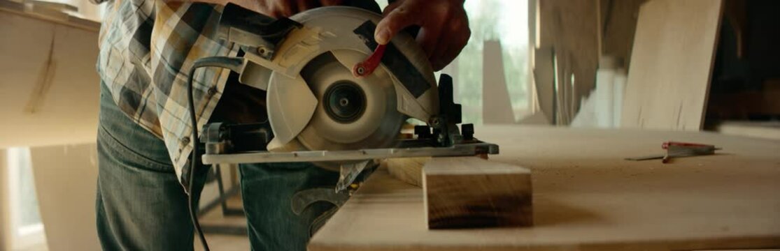CU Caucasian male using electric circular saw to make a canoe paddle in his workshop. Boat making hobby, small business owner. Shot on RED Dragon
