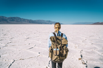 Back view of female traveler using smartphone camera for making selfie on scenic background of Death Valley,woman carrying backpack having journey in Badwater national park taking picture on mobile