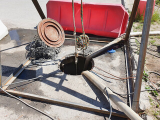 An open sewer manhole and a red guardrail. Repair work.