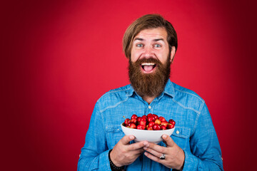 happy bearded man with sweet cherry. cherries for breakfast. cheerful male hipster hold fresh berry. fruit full of vitamin. only organic food. dieting and healthy lifestyle