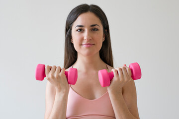 Young brunette woman exercising with pink dumbbells in front of a white background