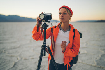 Concentrated female photographer making settings before shooting vieo of scenic nature of Badwater national park in USA, skilled woman taking pictures of landscape of dry lake in Death Valley .