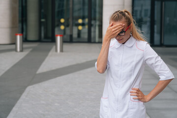 Fototapeta premium A brooding doctor with glasses in a white robe. Woman doctor the background of the medical clinic