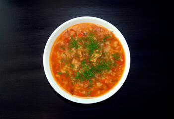 Kharcho soup in a white bowl on dark wooden background. Top view. Famous traditional Georgian kharcho soup with beef, rice and tomatoes. Georgian lamb and rice soup