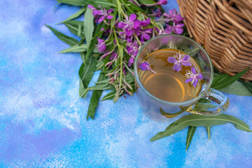 Traditional Russian herbal drink Ivan tea in a transparent cup.
Close-up, leaves of Ivan tea, fireweed, wicker basket background.
