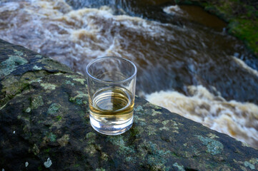 Scotch single malts or blended whisky spirits in glasses with water of river Spey on background,...