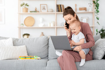 Balancing Work And Motherhood. Woman using cellphone and laptop while holding baby