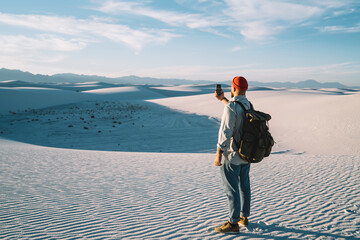 Hipster guy wanderlust making selfie on smartphone camera on breathtaking scenery of desert back...