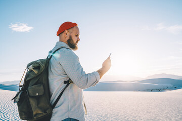 Young hipster guy checking application notification navigating via smartphone and good mobile data connection in White sands desert, male traveler exploring scenery places using internet in roaming