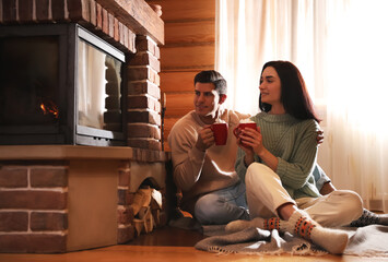 Lovely couple with delicious cocoa near fireplace on floor at home. Winter vacation