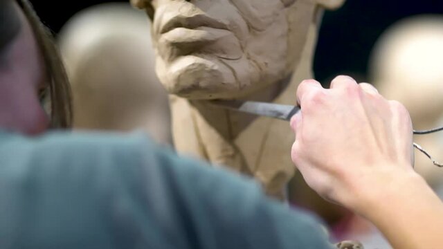 Woman sculptor at work on a sculpture of a human head. The process of restoring the shape of the neck. Side view. Close up view.