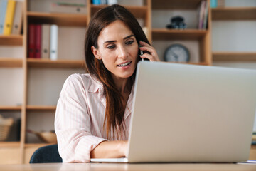 Image of businesswoman talking on mobile phone while working with laptop