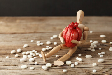 Toy man holds an anatomical heart in his hands, sits next to pills. Cardiovascular system treatment, heart attack prevention.