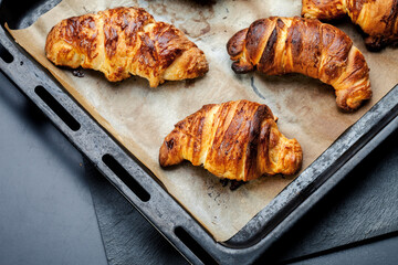 Oven-baked sugar-frosted croissants on a baking sheet covered with parchment paper. Sweet bagels from a cottage cheese dough baked in a hot oven. The process of making curd bagels or croissants