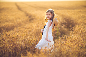 Fototapeta na wymiar Fashion photo of a little girl in white dress and straw hat at the evening wheat field.